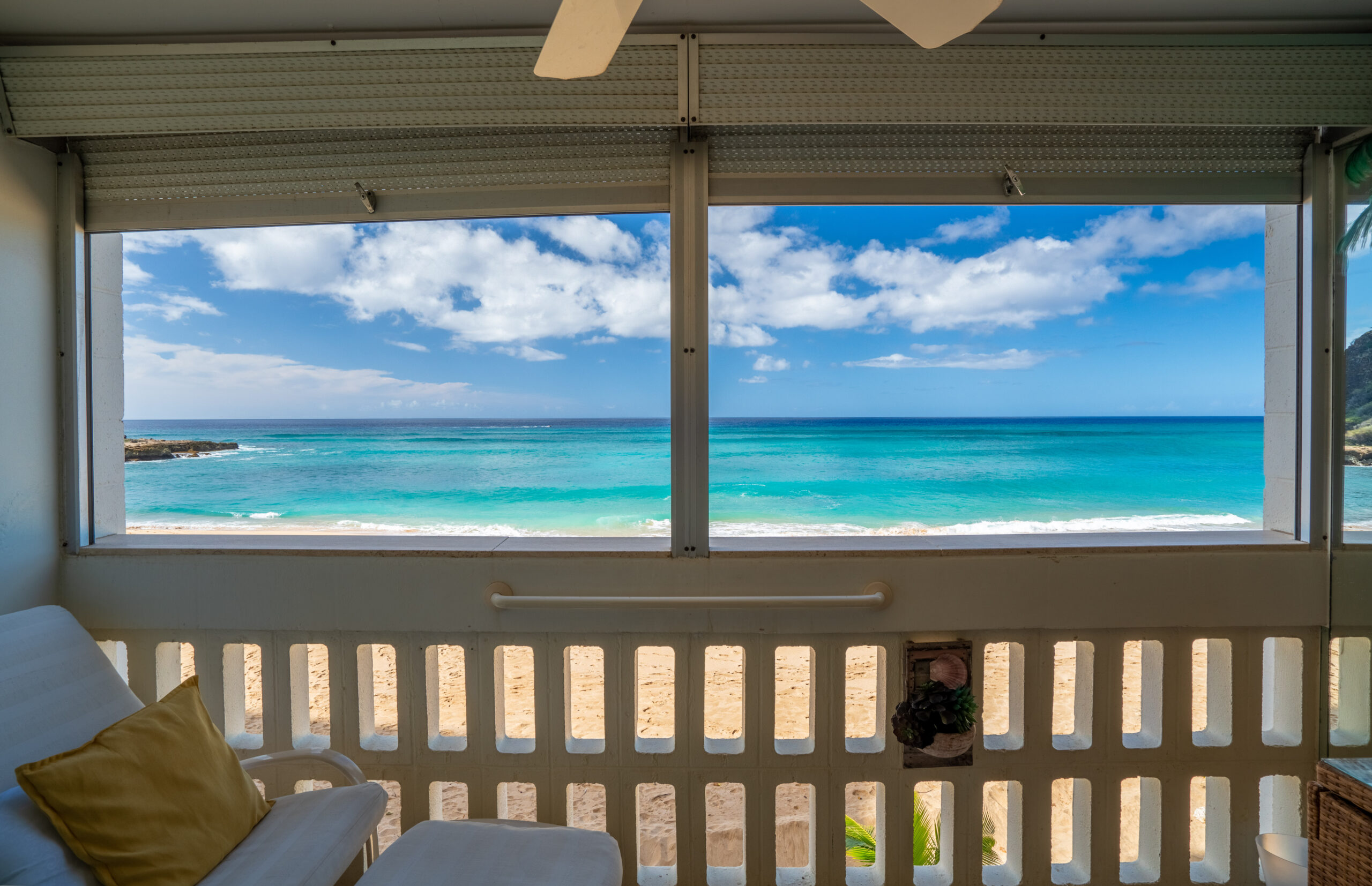 Ocean view from a beachside balcony, featuring a turquoise sea, sandy shore, and partly cloudy skies, perfect for relaxation and coastal vibes.
