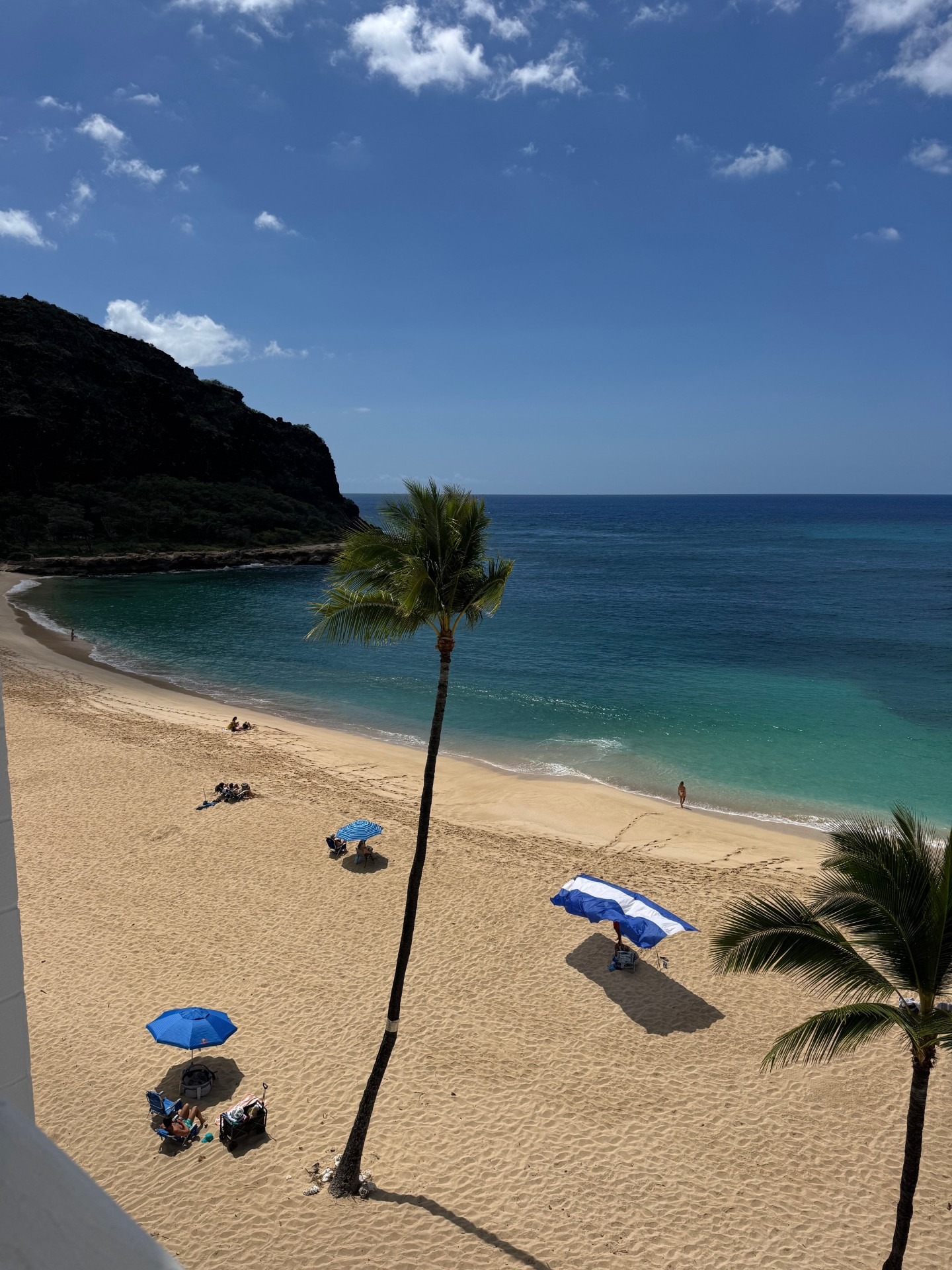 Calm beach scene with turquoise waters, golden sand, and a few sunbathers under a blue umbrella, showcasing a relaxing coastal getaway.