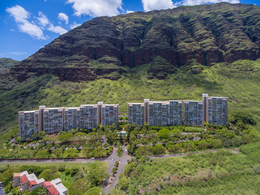 Mākaha Valley Tower entrance surrounded by tropical plants and colorful flowers, highlighting a peaceful residential area in Hawaii.