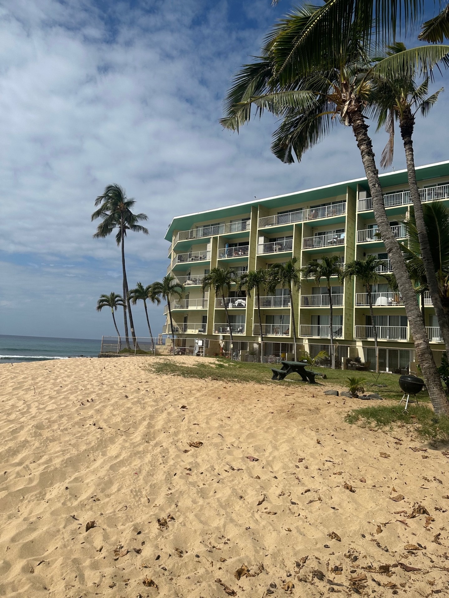 Makaha Shores building nestled among palm trees, featuring a modern sign. The well-maintained lawn enhances the tropical atmosphere.