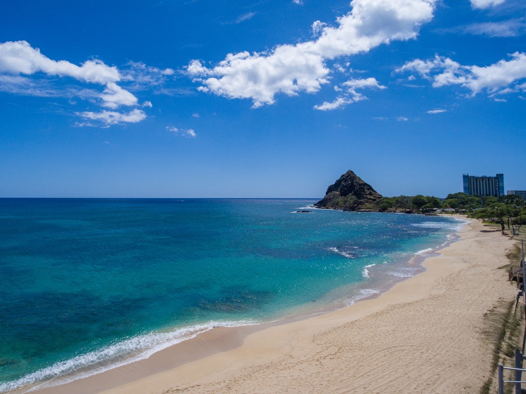 A pristine beach with turquoise water, a rocky hill, and a clear blue sky in the background.